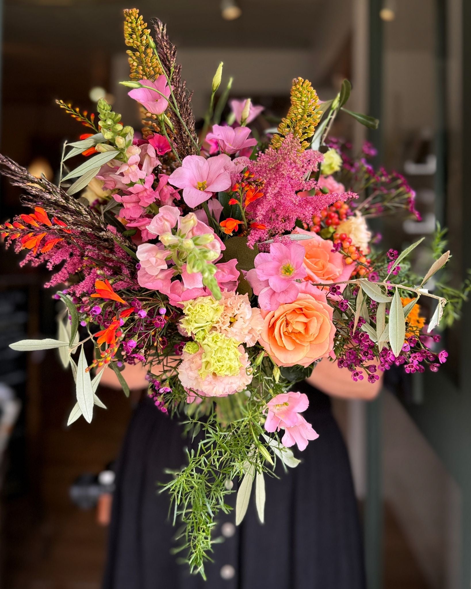 Bouquet of colorful flowers held by a person in a blurred indoor setting