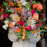 Bouquet of colorful flowers held by a person wearing a light-colored coat.