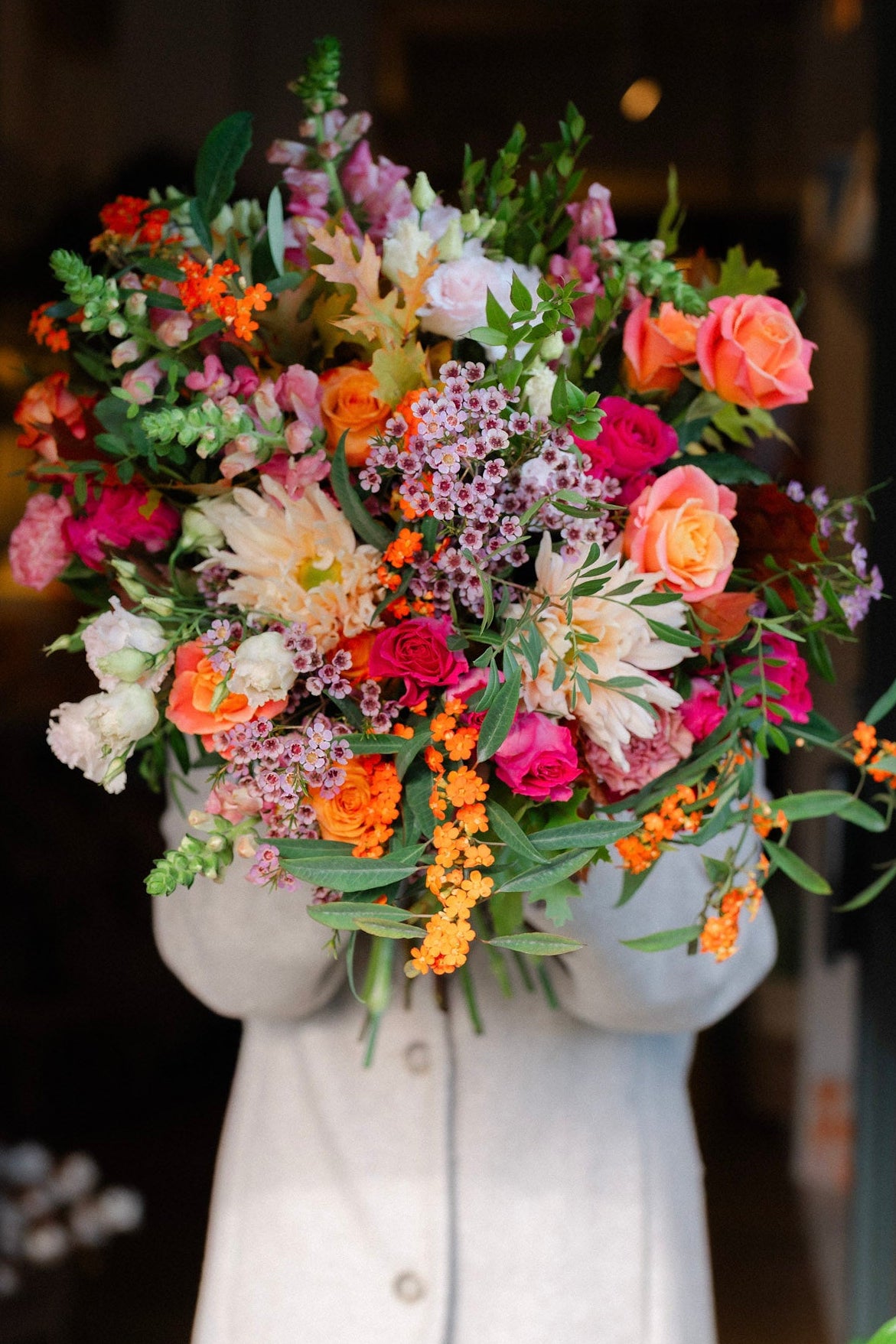 Bouquet of colorful flowers held by a person wearing a light-colored coat.