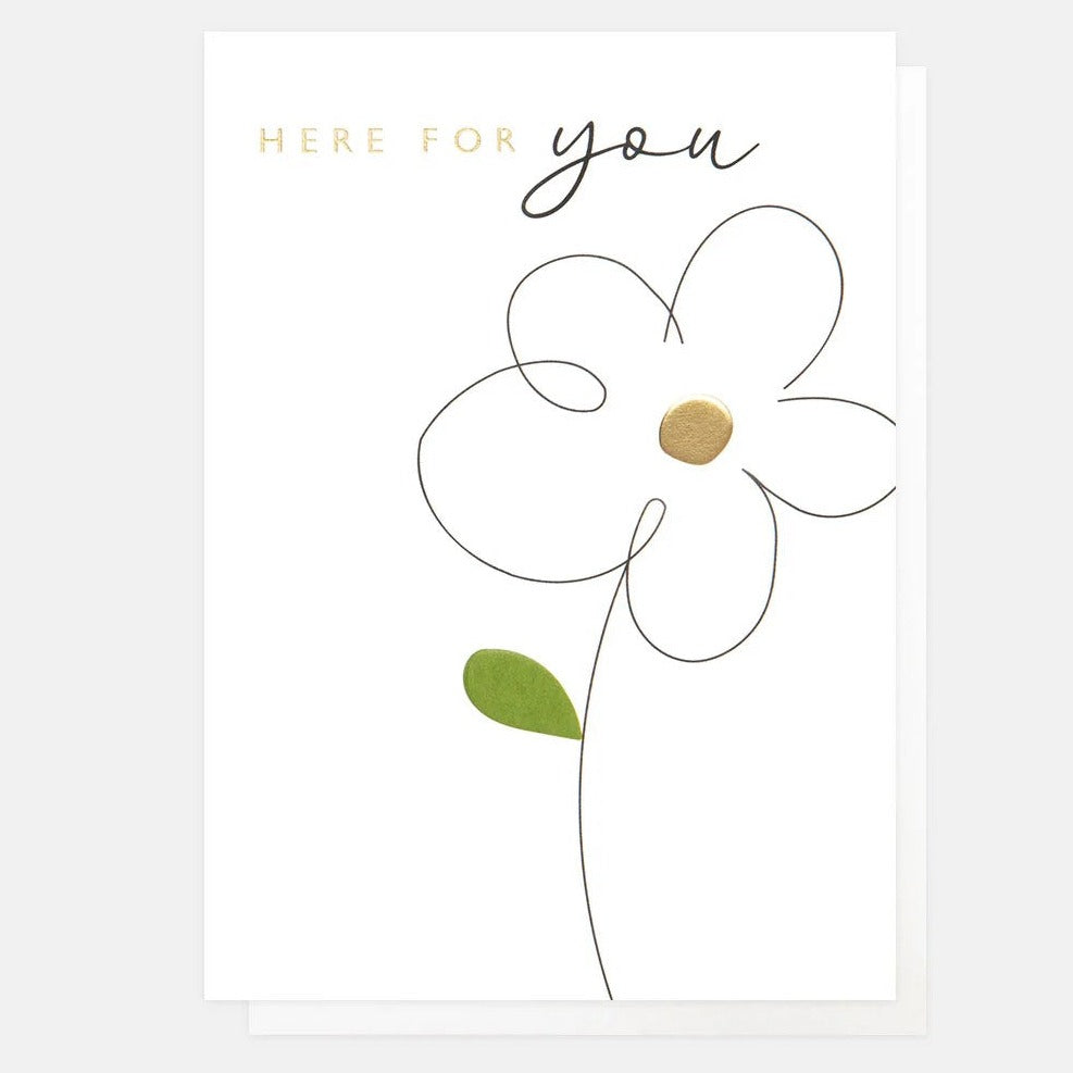 A greeting card with a white background featuring a gold foil daisy flower and the text 'HERE FOR YOU' on the right side, accompanied by a small green leaf design.