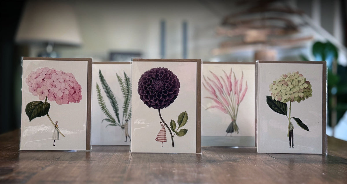 Five card designs with floral and botanical illustrations on a wooden surface.