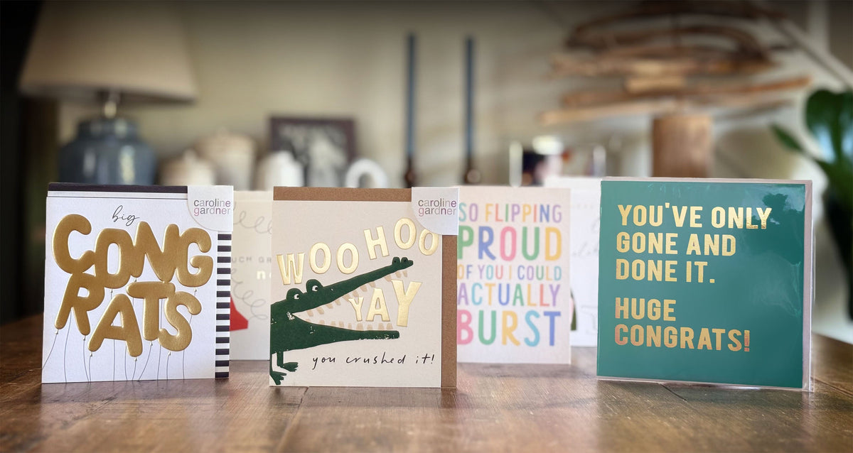 Four congratulation cards with different messages on a wooden dining table.