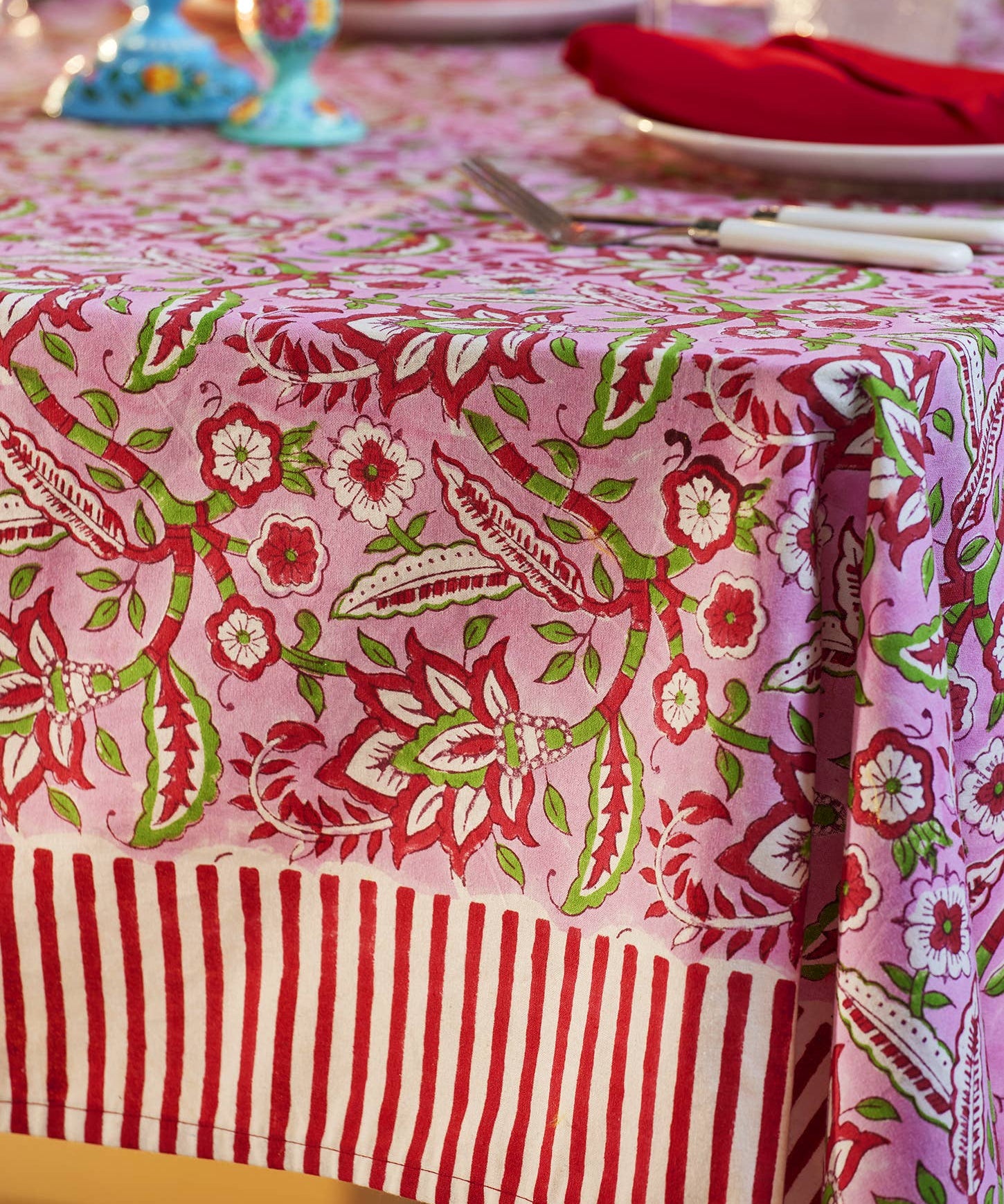 Pink floral block print cotton tablecloth with red and white candy stripe border styled for elegant dining and entertaining.