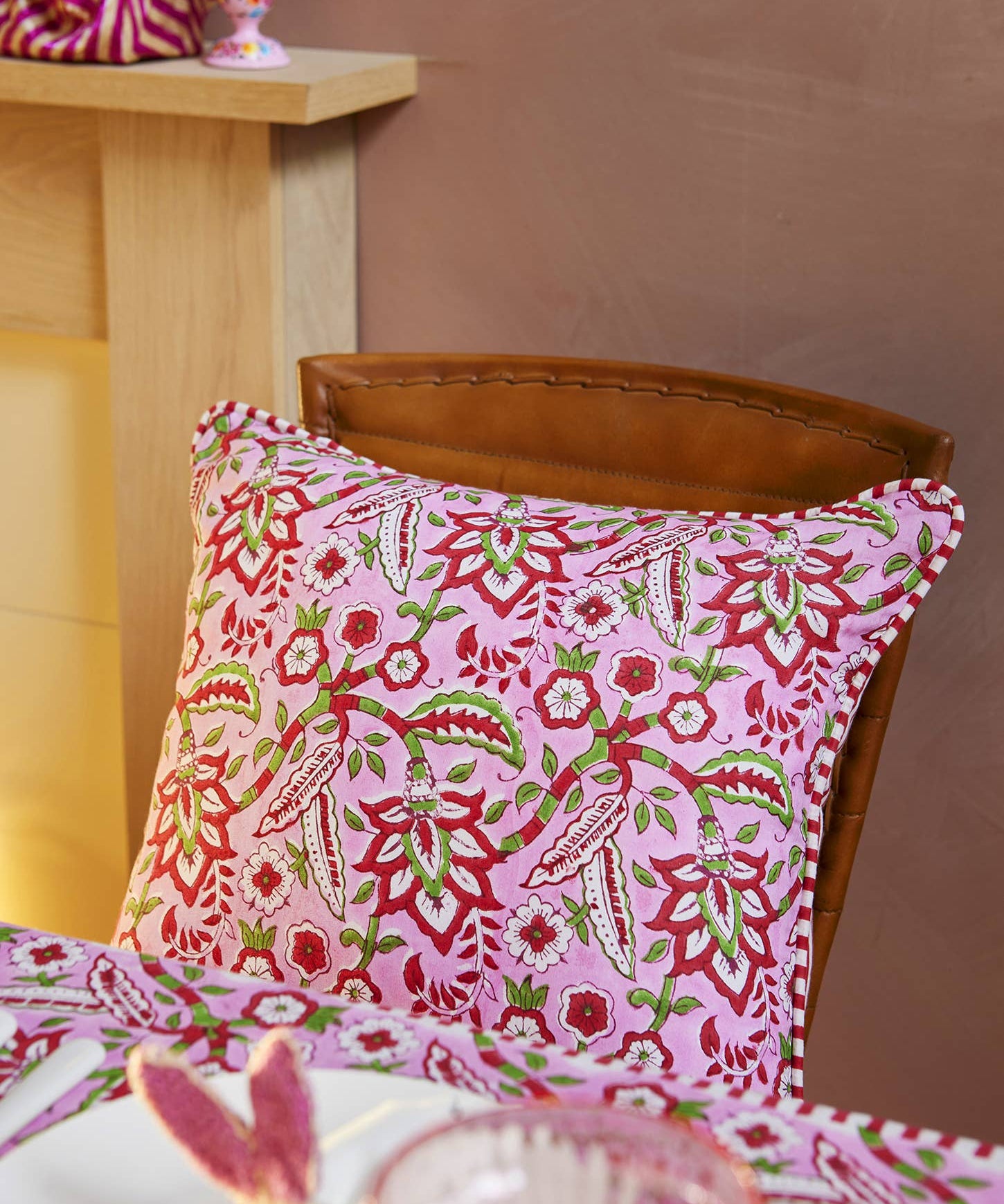 Pink floral block print cotton cushion cover with red striped reverse and decorative beaded edging styled on a sofa.