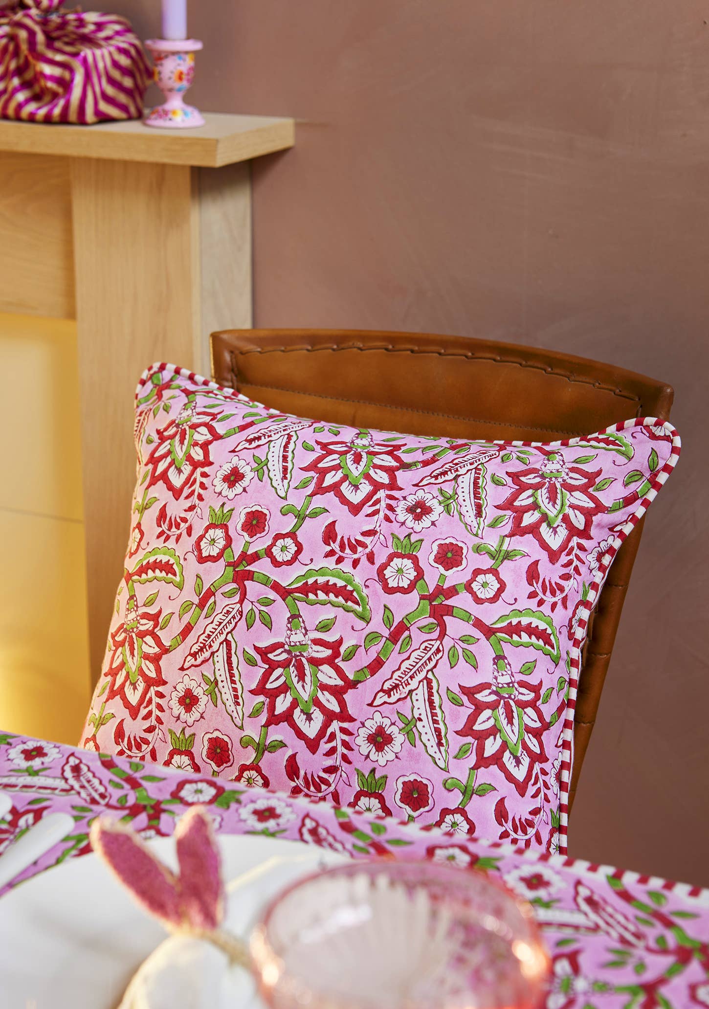 Pink floral block print cotton cushion cover with red striped reverse and decorative beaded edging styled on a sofa.