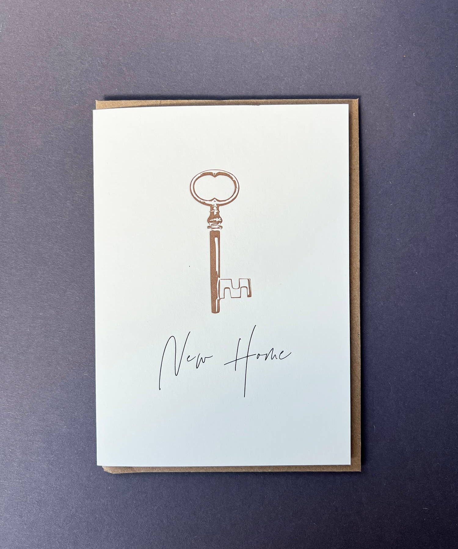 Penguin Ink New Home Key letterpress greeting card featuring a vintage key with metallic gold detailing and modern calligraphy, printed on 100% recycled board with a tactile embossed finish.