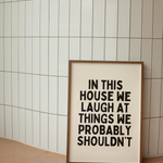 Framed poster with humorous text 'In this house we laugh at things we probably shouldn't' 
