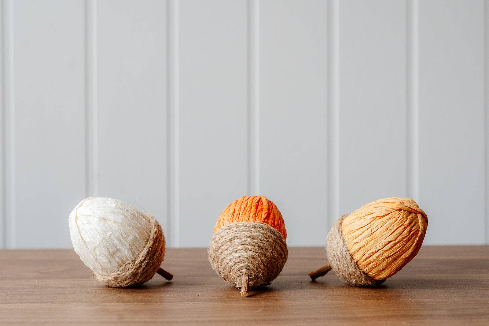 Decorative rope and paper acorns in cream, orange and yellow, styled in an autumn display with pumpkins and seasonal foliage.