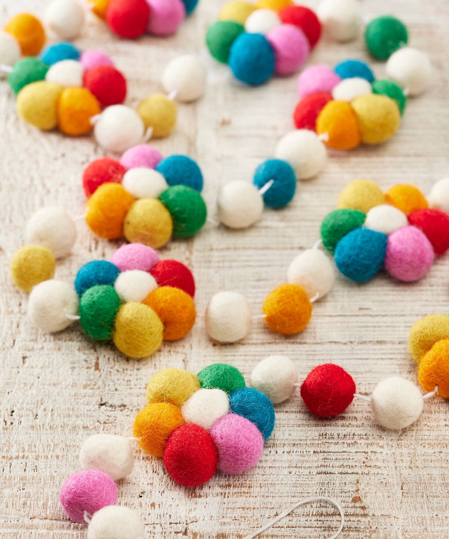 Colourful wool felt flower garland with felt ball details hanging as decorative reusable party and home décor.