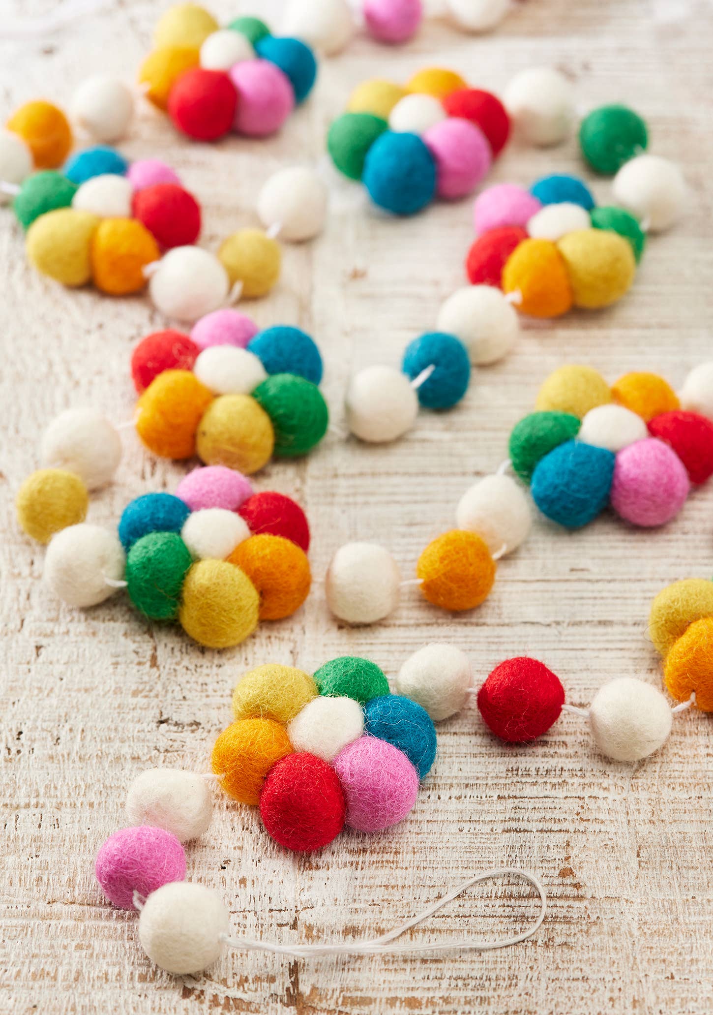 Colourful wool felt flower garland with felt ball details hanging as decorative reusable party and home décor.
