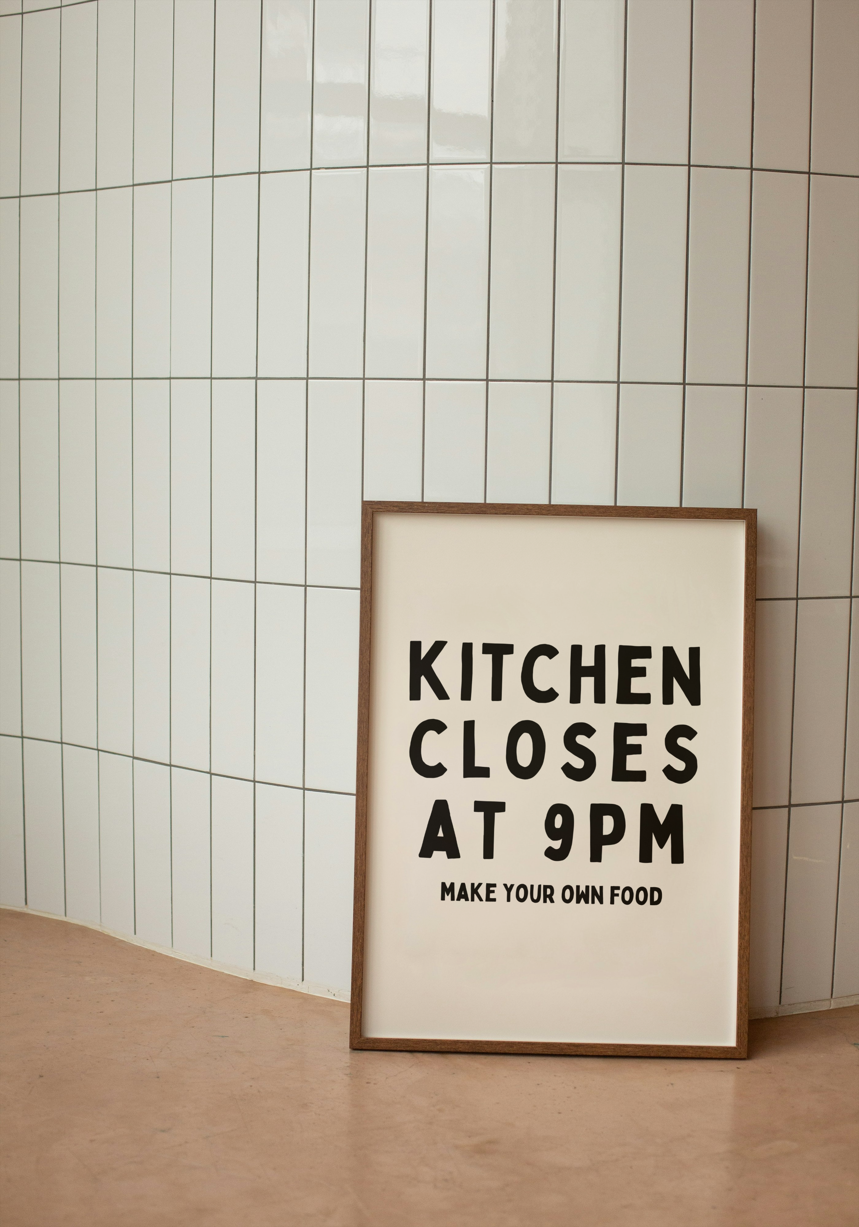 Framed poster with text 'Kitchen Closes at 9PM Make Your Own Food' against a tiled wall.