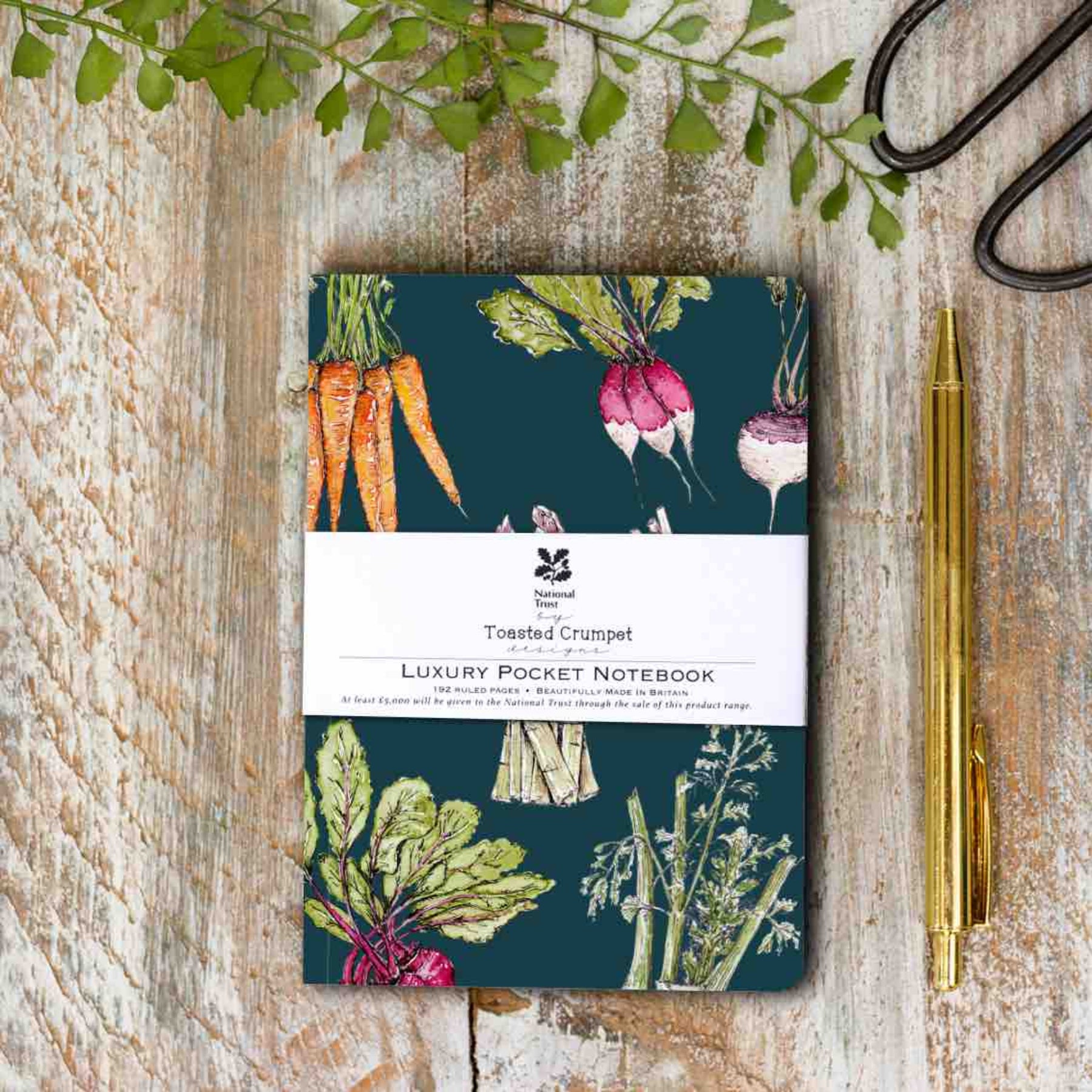 Luxury pocket notebook with vegetable design on a wooden surface with a pen and leaves.