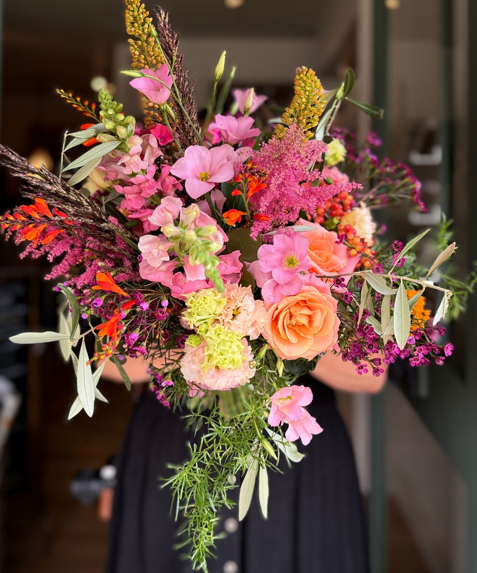 Bouquet of colorful flowers held by a person in a blurred indoor setting