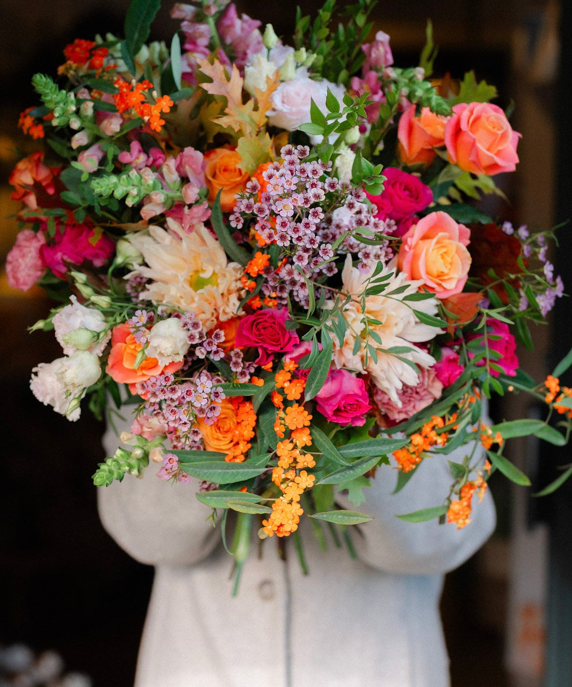 Bouquet of colorful flowers held by a person wearing a light-colored coat.