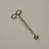 Stainless steel wick trimmer with a looped end and the True Grace emblem engraved on the handle