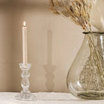 A clear glass candlestick with a decorative element 