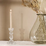 A clear glass candlestick with a decorative element 