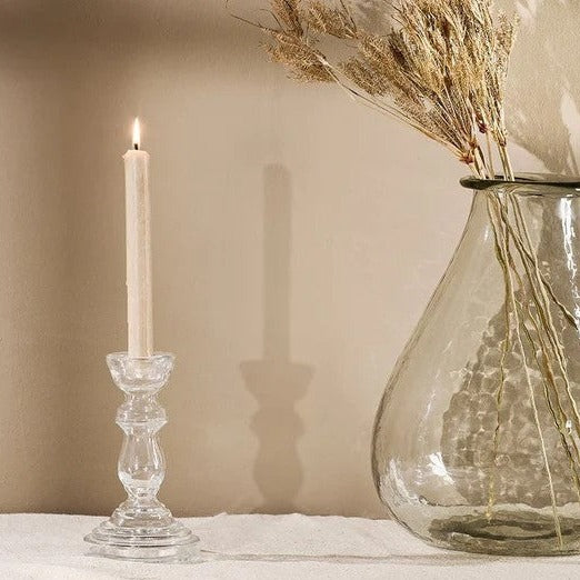 A clear glass candlestick with a decorative element 