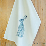 A white cotton tea towel with an illustration of a blue hare (rabbit) on it