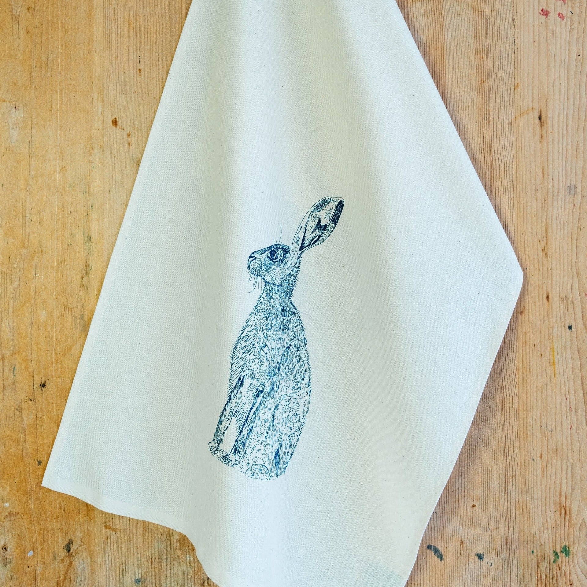 A white cotton tea towel with an illustration of a blue hare (rabbit) on it
