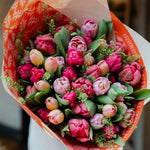 Bouquet of pink tulips wrapped in orange paper held by a person.
