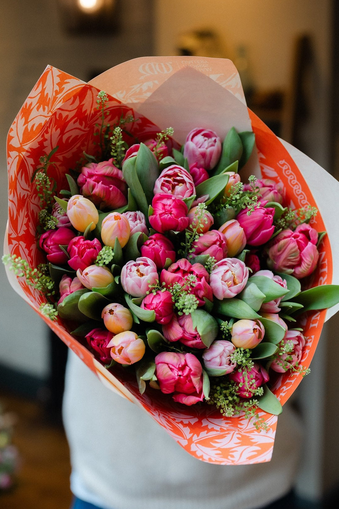 Bouquet of pink tulips wrapped in orange paper held by a person.