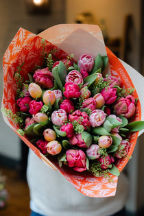 Bouquet of pink tulips wrapped in orange paper held by a person.