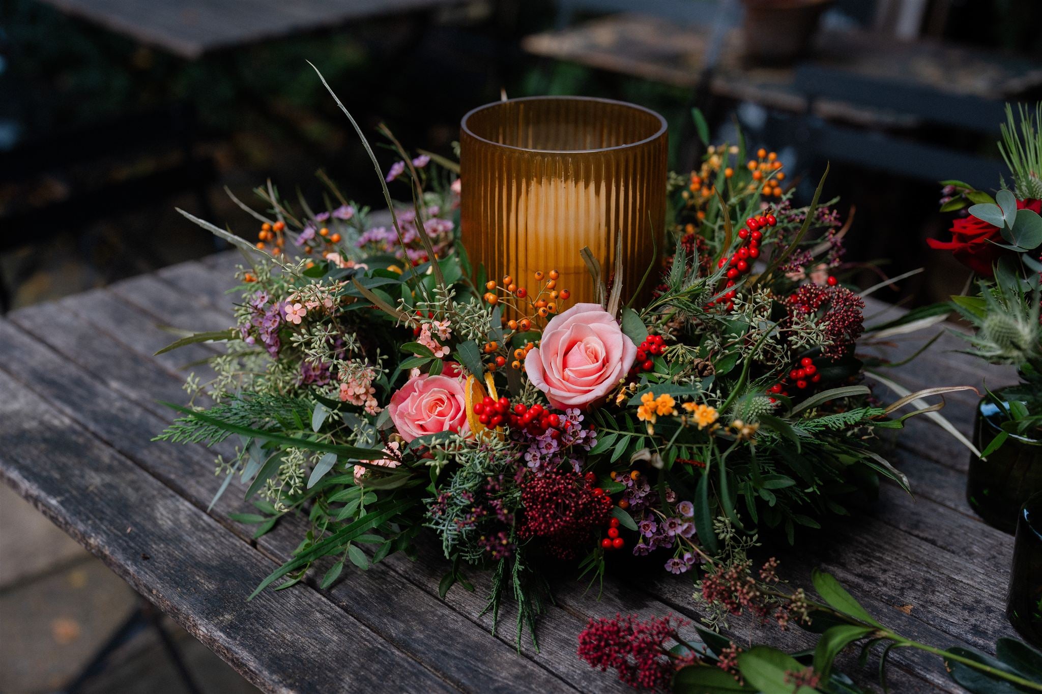 Meet The Tipsy Truffle, a luxury Christmas table centrepiece with dusky pink roses, winter berries, festive foliage and an elegant hurricane candle holder.
