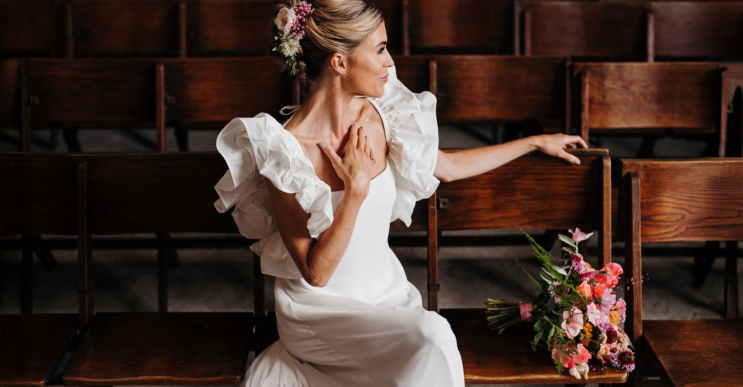 Woman in a white wedding dress sitting in a church pew with her bridal flowers.
