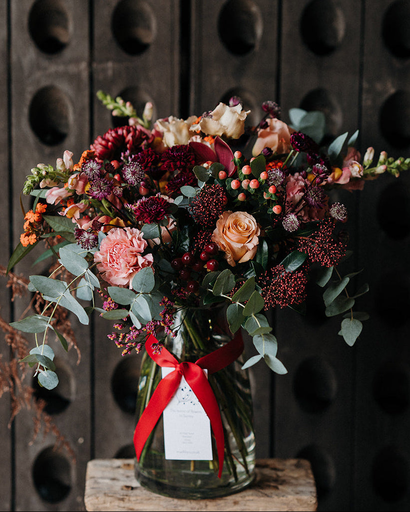 The Cherry Brandy luxury Christmas vase arrangement featuring rich warm burgundy and soft apricot seasonal flowers with textured winter foliage.