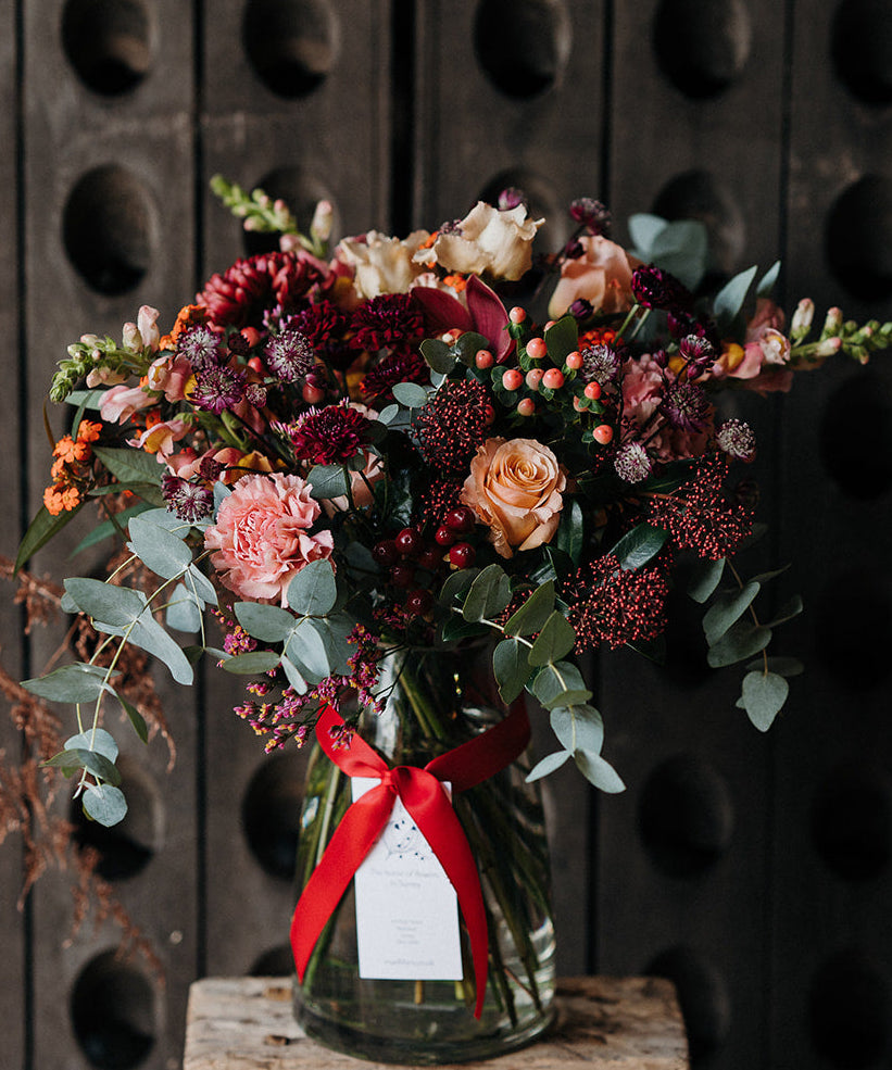 The Cherry Brandy luxury Christmas vase arrangement featuring rich warm burgundy and soft apricot seasonal flowers with textured winter foliage.