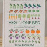 Book titled 'Veg in One Bed' by Huw Richards on a wooden surface with a plant in the background.
