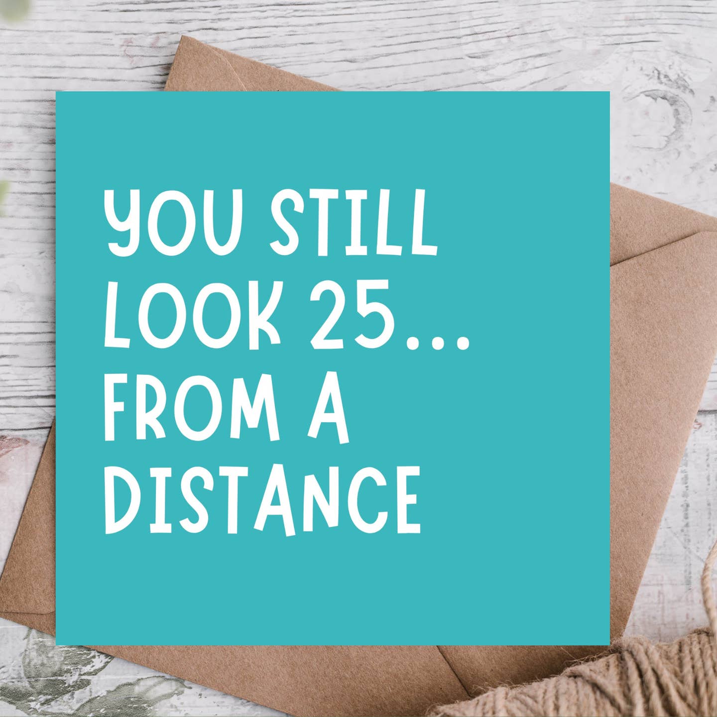 Teal card with white text 'You still look 25... from a distance' on a wooden surface.