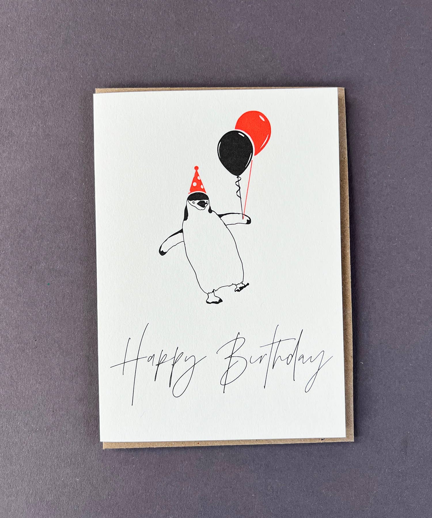 Penguin Ink Happy Birthday Penguin letterpress card featuring a chinstrap penguin wearing a neon spotty party hat and holding balloons, printed on 100% recycled board with an embossed finish.