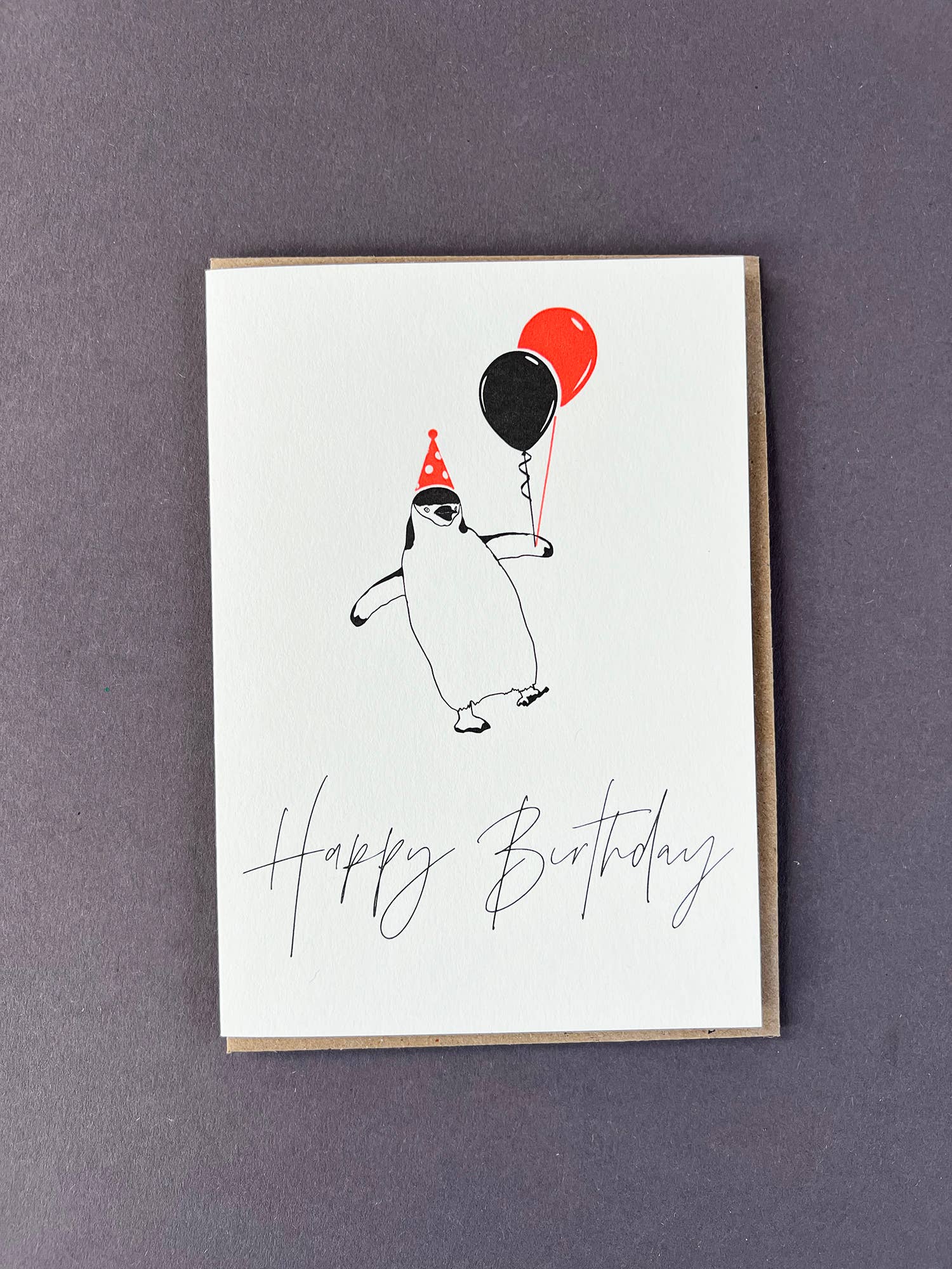 Penguin Ink Happy Birthday Penguin letterpress card featuring a chinstrap penguin wearing a neon spotty party hat and holding balloons, printed on 100% recycled board with an embossed finish.