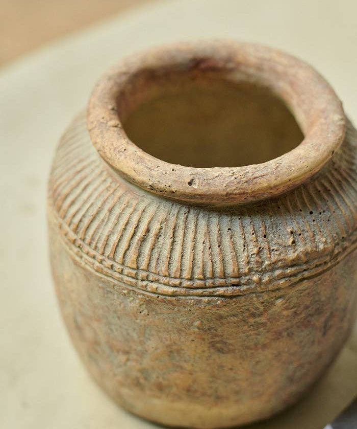 Abigail Ahern Tamil cement vase with a textured matt finish and sculptural rounded silhouette, styled with faux stems in a contemporary interior.