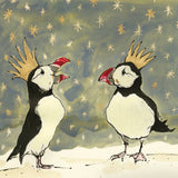 Anna Wright Christmas Puffins card featuring two illustrated puffins wearing golden party hats beneath a starlit sky.