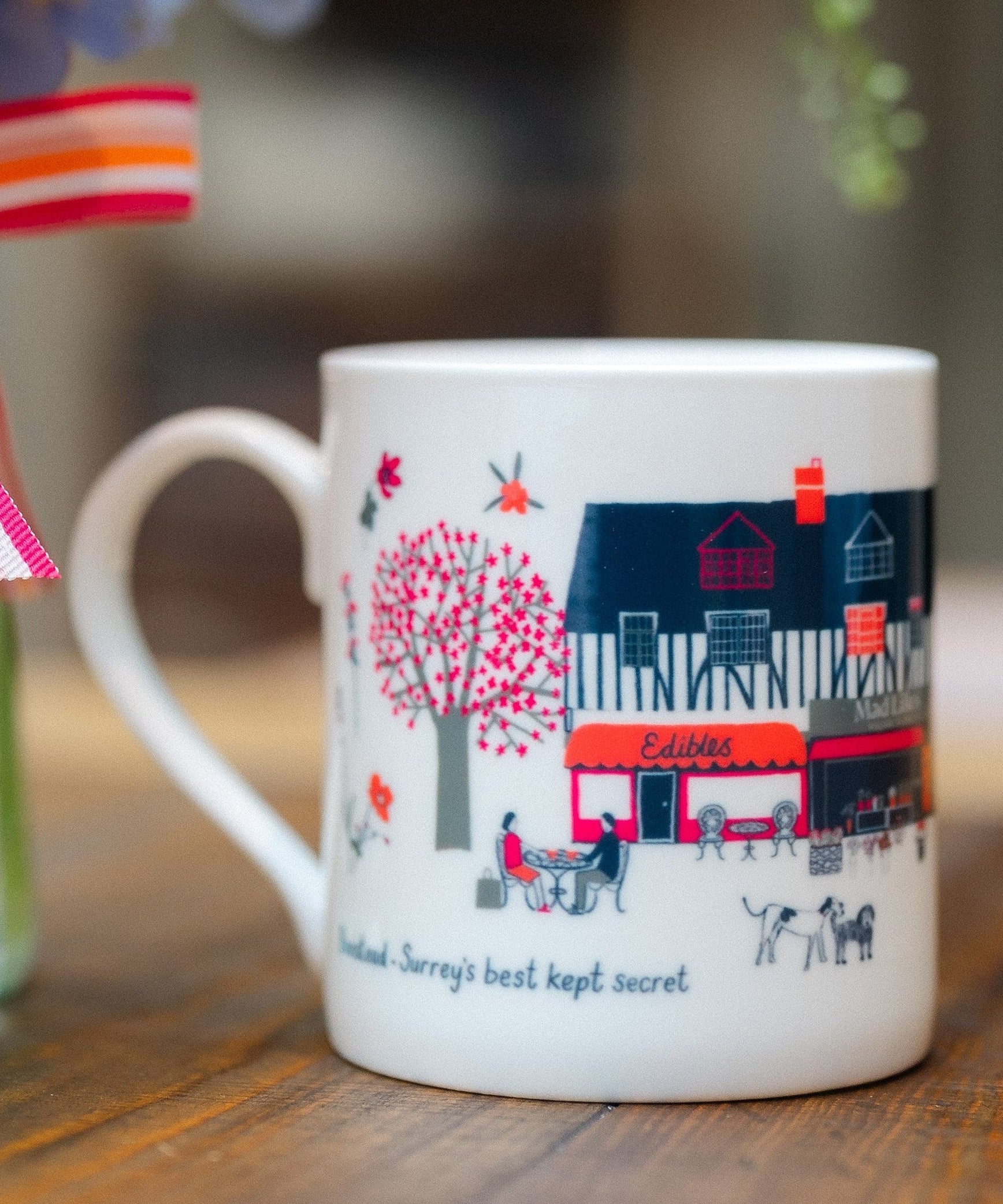 Banstead Village Life ceramic mug featuring colourful illustrations of Banstead High Street, independent shops and village landmarks by Surrey artist Lisa Tolley.