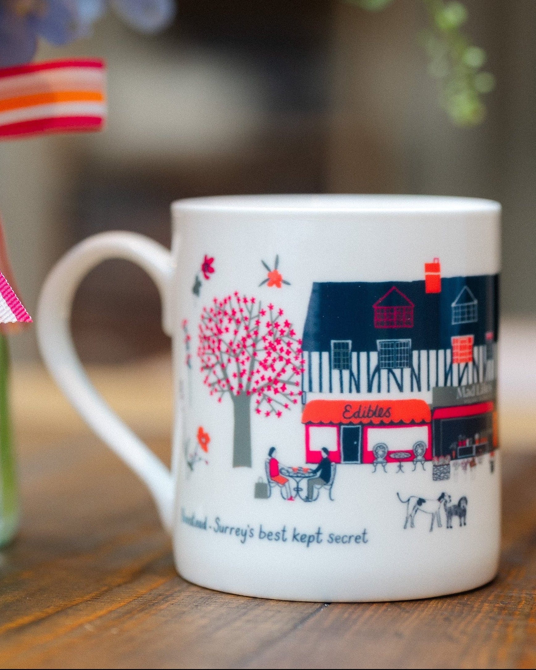Banstead Village Life ceramic mug featuring colourful illustrations of Banstead High Street, independent shops and village landmarks by Surrey artist Lisa Tolley.