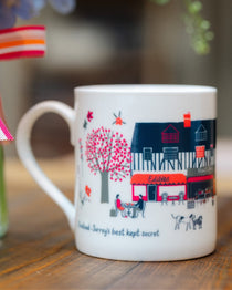Banstead Village Life ceramic mug featuring colourful illustrations of Banstead High Street, independent shops and village landmarks by Surrey artist Lisa Tolley.
