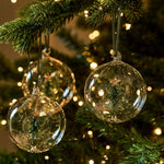 Set of three clear glass Christmas baubles with green Christmas trees suspended inside and dark green hangers