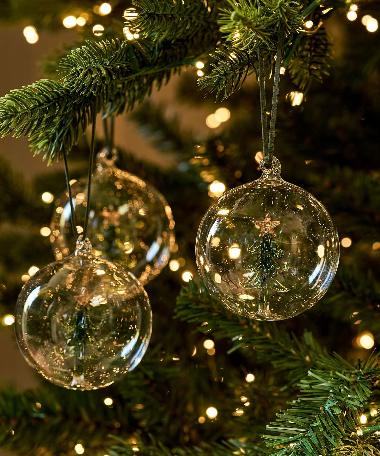Set of three clear glass Christmas baubles with green Christmas trees suspended inside and dark green hangers