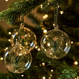Set of three clear glass Christmas baubles with green Christmas trees suspended inside and dark green hangers