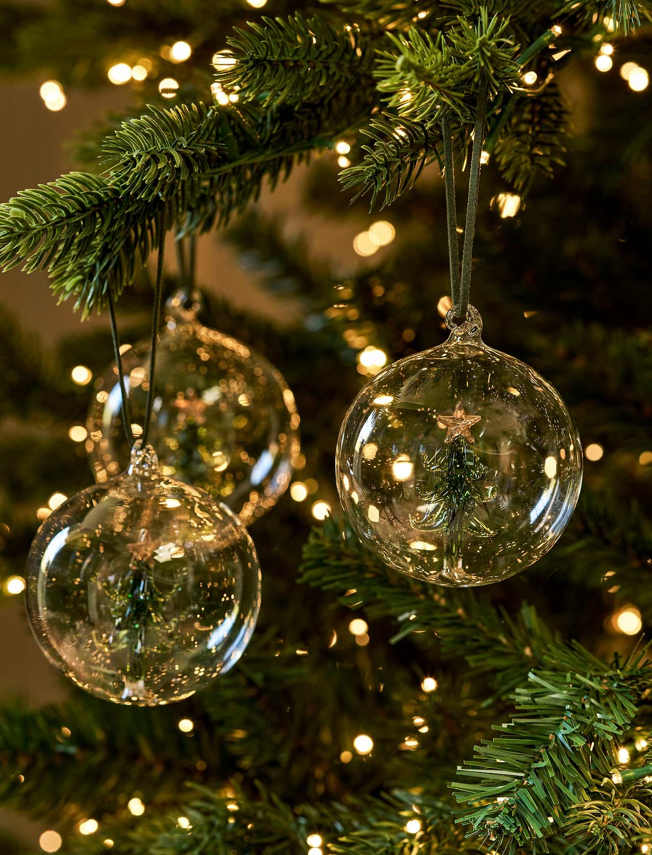 Set of three clear glass Christmas baubles with green Christmas trees suspended inside and dark green hangers