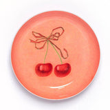 Handmade round cherry enamel trinket dish with a vintage-inspired cherry illustration on a rich red enamel background.