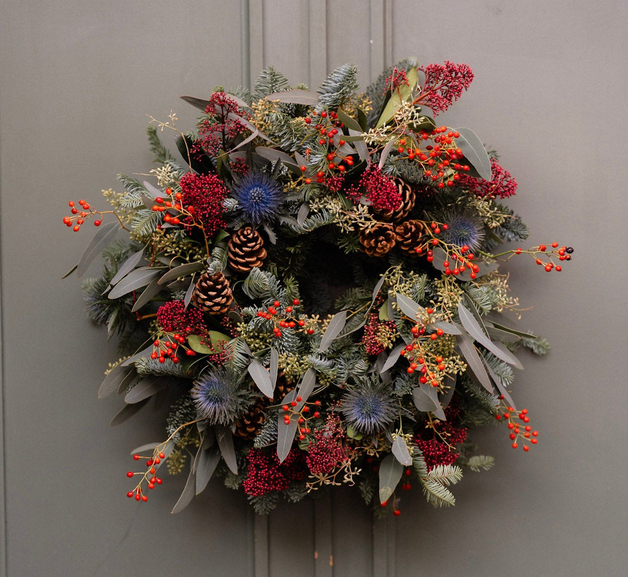 Decorative wreath with greenery, berries, and pinecones on a plain background