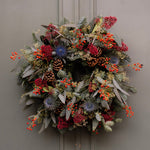 Decorative wreath with greenery, berries, and pinecones on a plain background