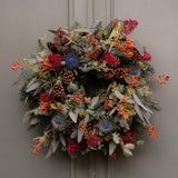 Decorative wreath with greenery, berries, and pinecones on a plain background