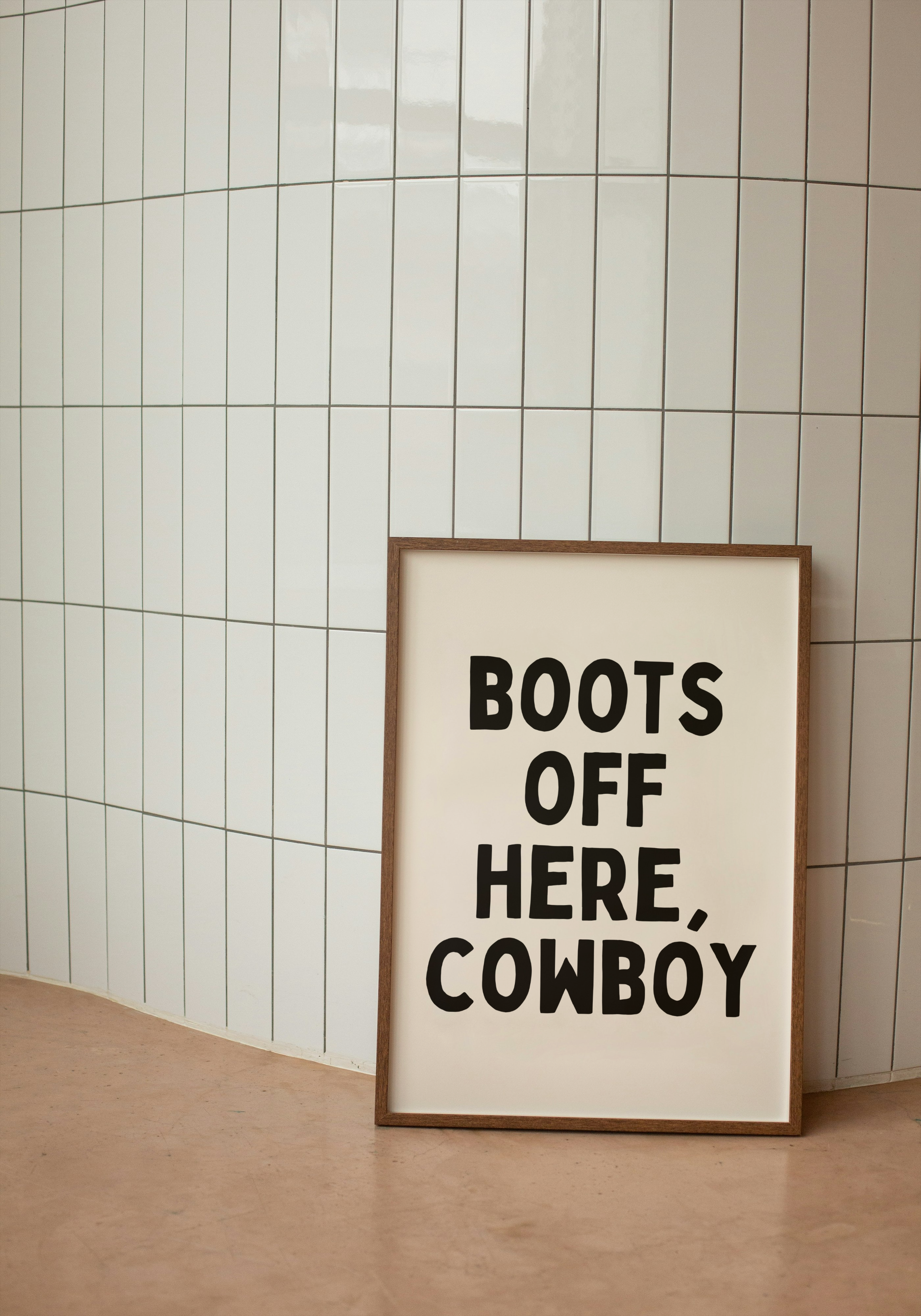 Framed poster with 'Boots Off Here, Cowboy' text against a tiled wall.