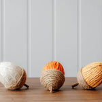 Decorative rope and paper acorns in cream, orange and yellow, styled in an autumn display with pumpkins and seasonal foliage.